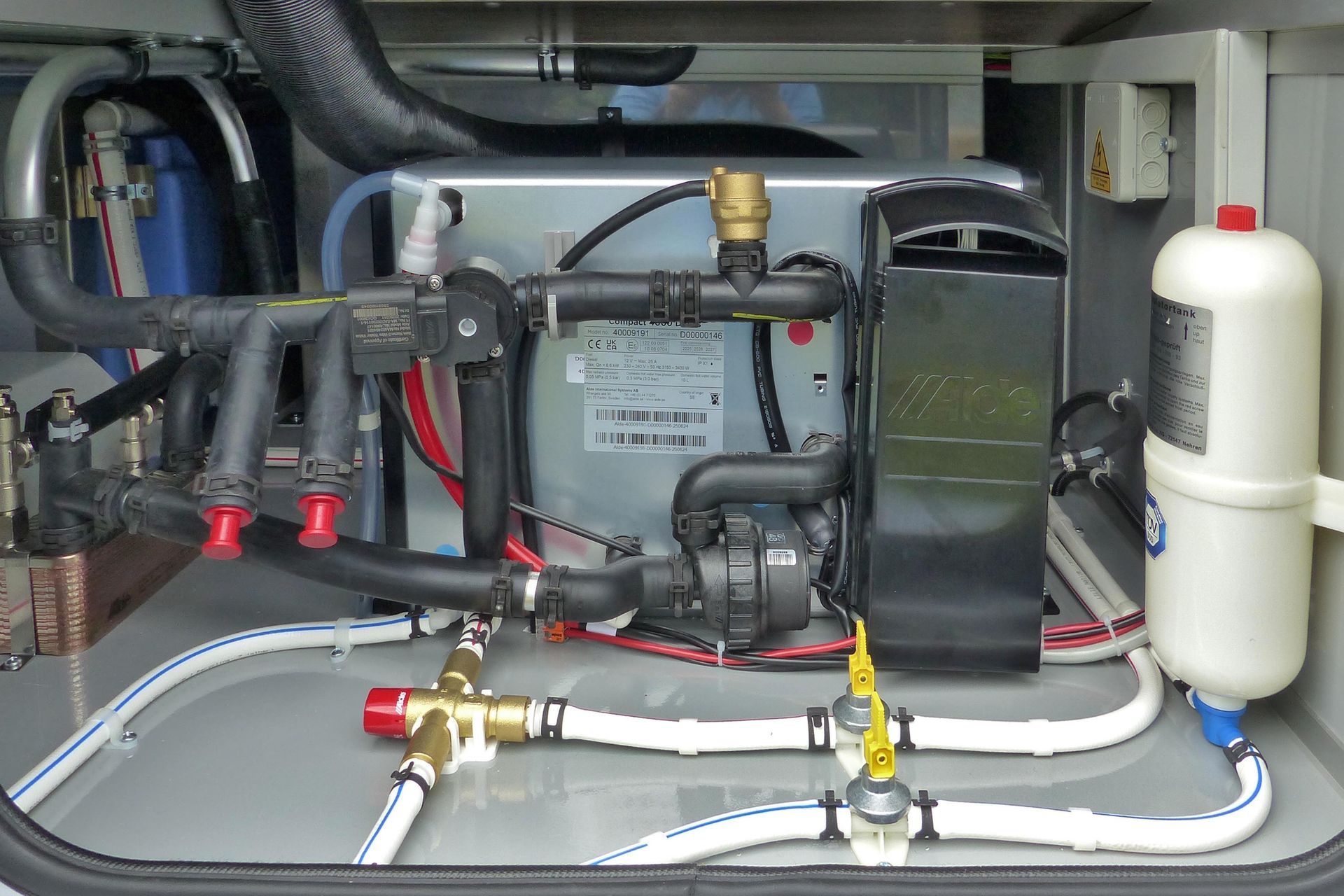 Wohnmobil-Warmwasserbereiter und -Installationen. Schwarze, silberne und weiße Komponenten mit roten und gelben Ventilen.