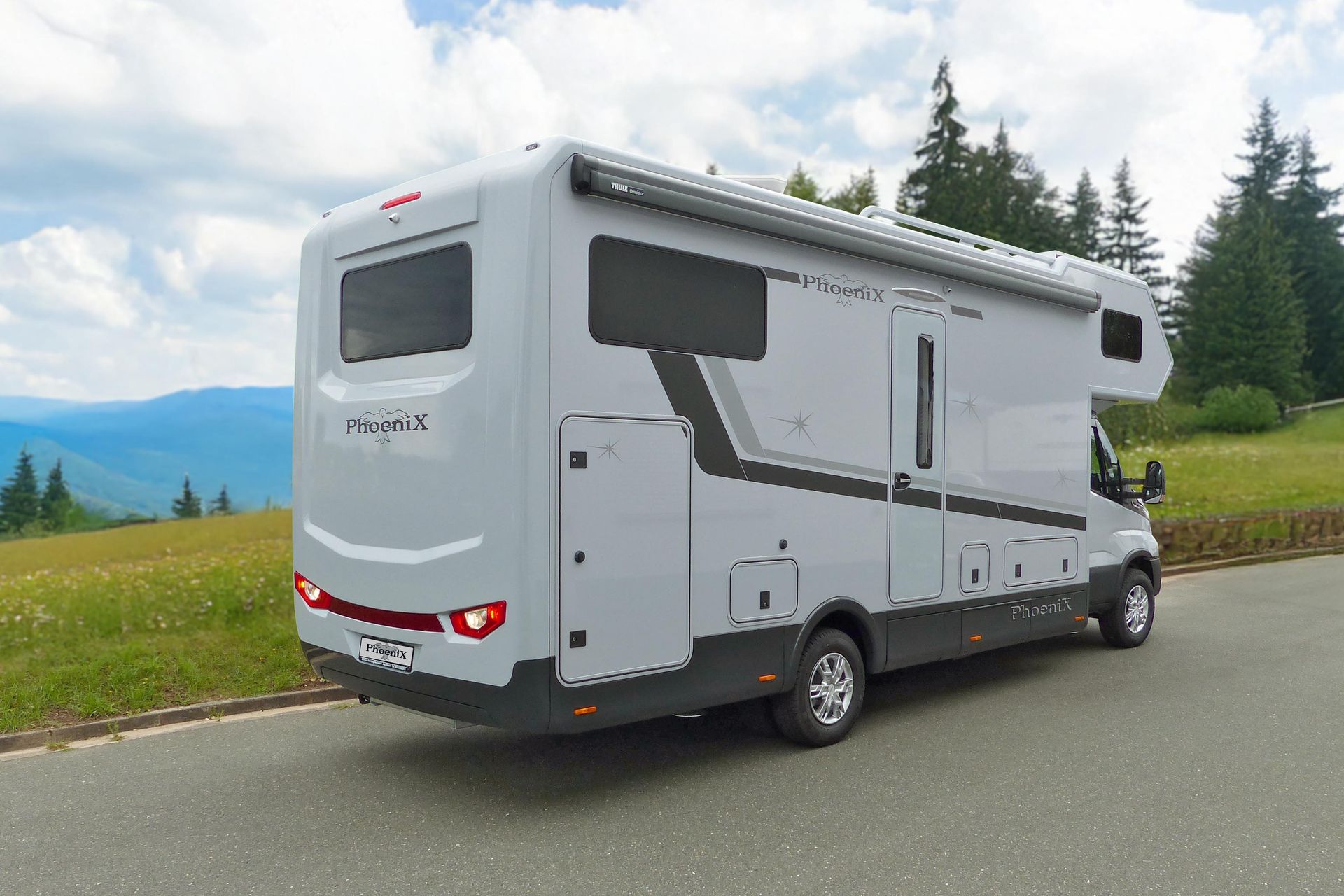 Graues Wohnmobil auf einer kurvenreichen Straße, Berge und Bäume im Hintergrund.