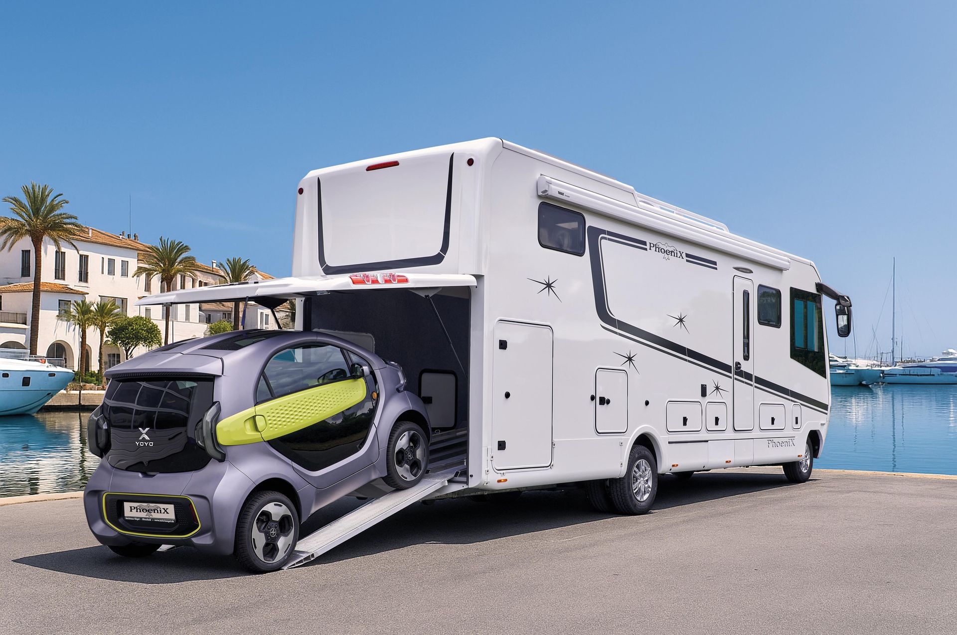 Ein großes weißes Wohnmobil mit einem kleinen grauen Auto in seiner Lagerbucht in der Nähe eines Hafens.
