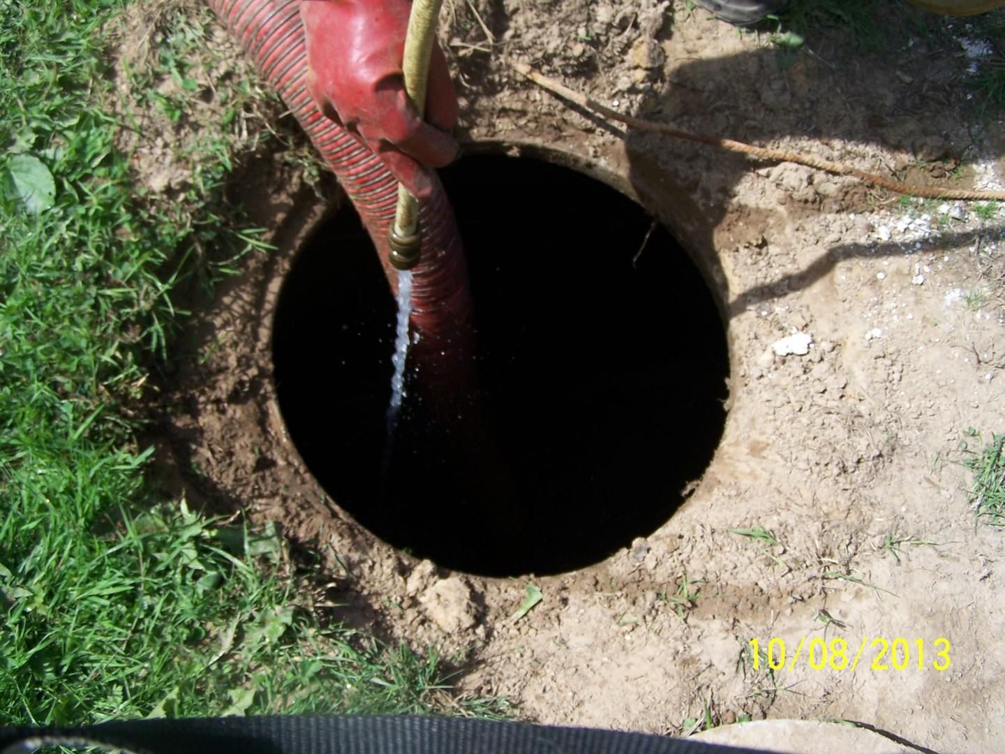 Un tuyau rouge pompe de l'eau dans un trou rond et sombre creusé dans le sol.