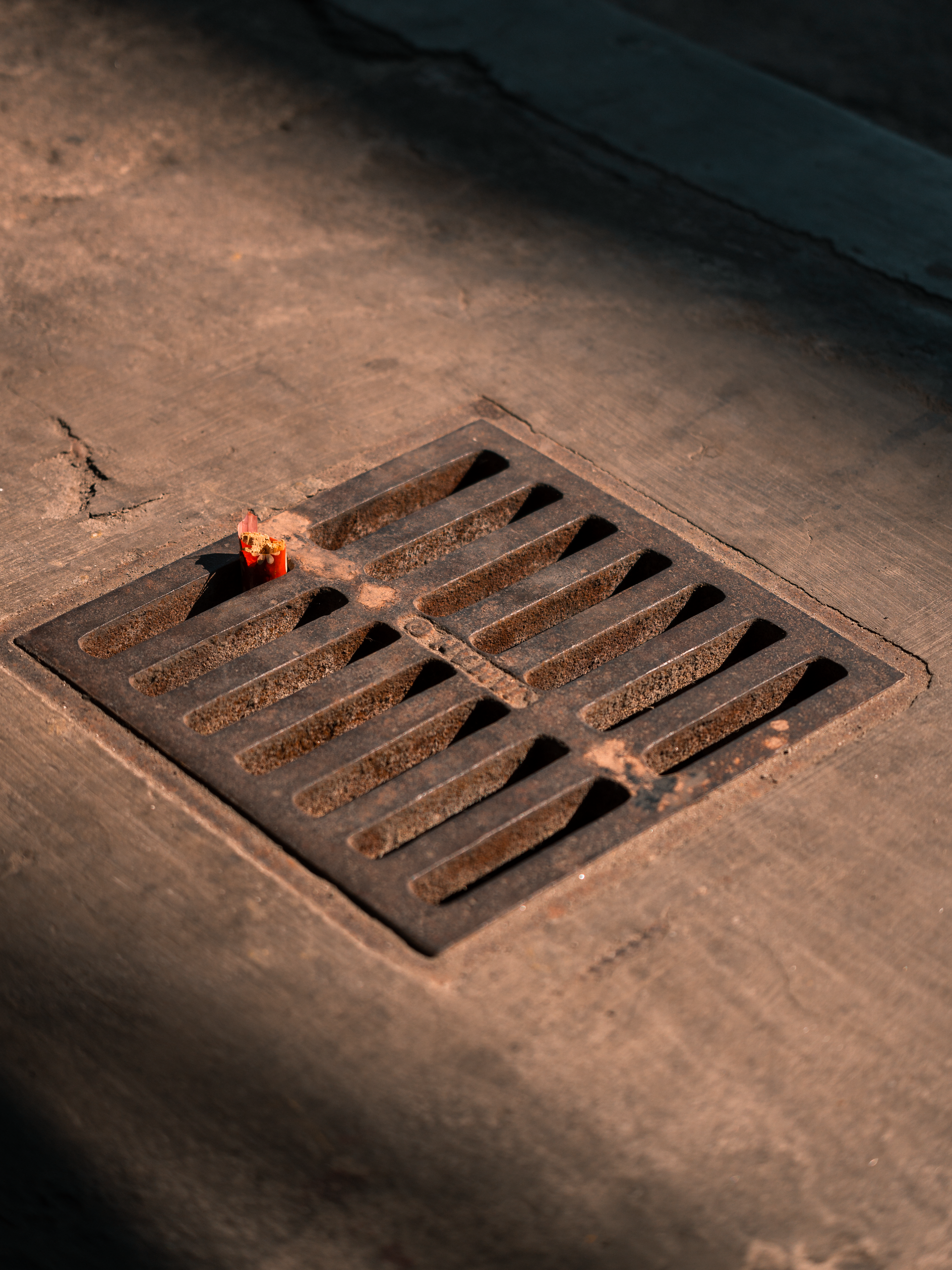 Grille d'évacuation en métal sur une surface en béton faiblement éclairée.