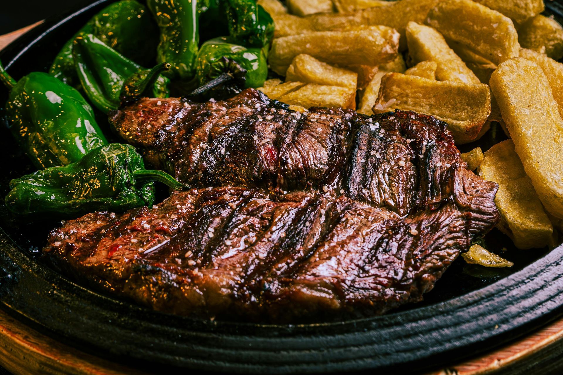 Bistec a la parrilla con patatas fritas y pimientos verdes en un plato negro.