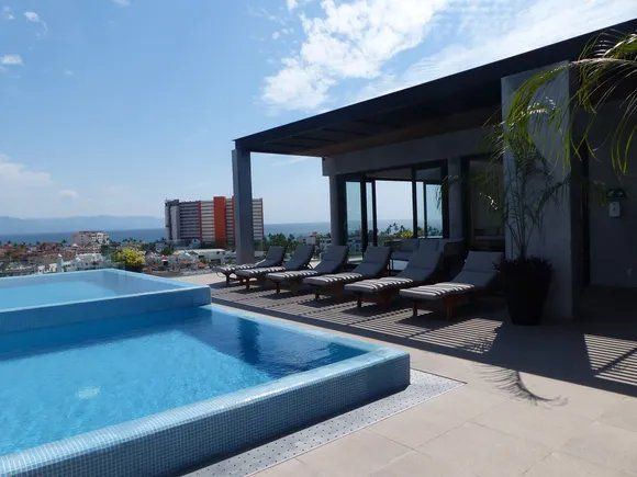 Rooftop pool and lounge area with ocean view under a sunny sky.