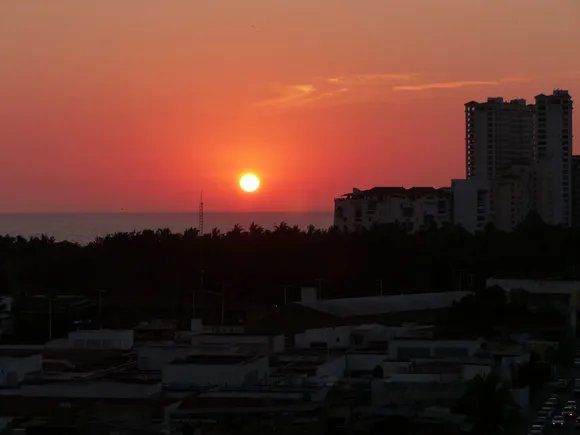 Fiery sunset over buildings and trees; orange sky, dark silhouettes.
