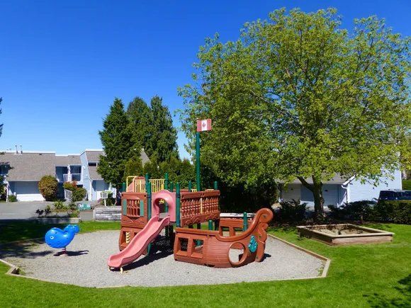 Playground with a slide, climbing structure, and sandbox on a grassy area, clear blue sky.