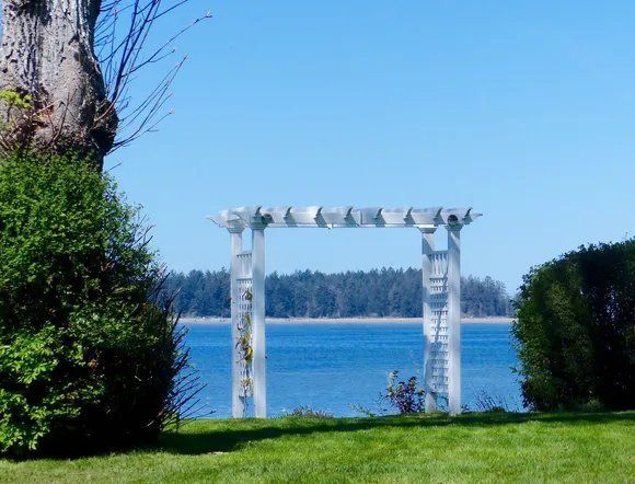 White arbor frames water and trees on a sunny day.