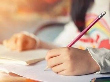 Enfant écrivant dans un cahier avec un crayon rose à un bureau