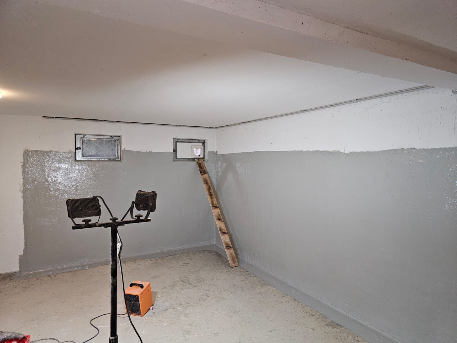 Ein Raum mit grauen Wänden, der gestrichen wird; an einer Wand lehnt eine Leiter.