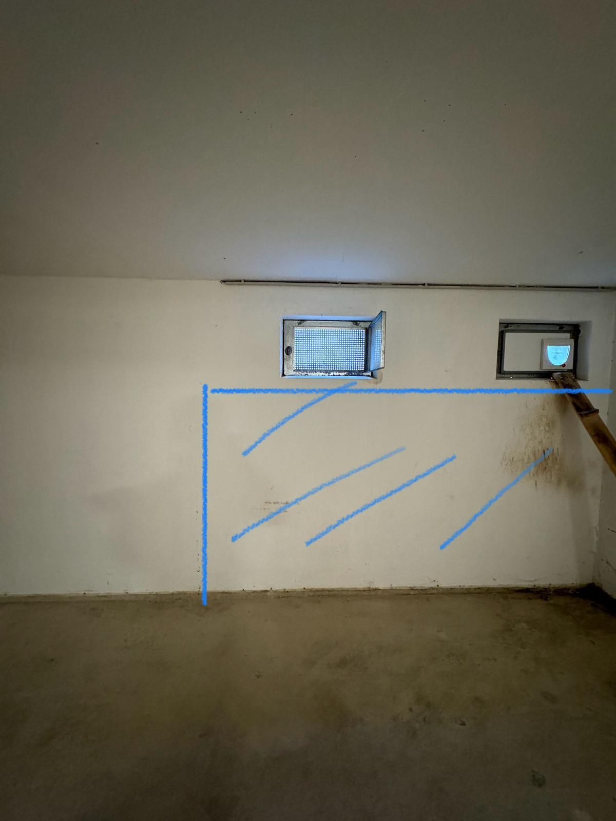 Kellerwand mit zwei Fenstern, die Wand ist weiß mit blauen Linien darauf.
