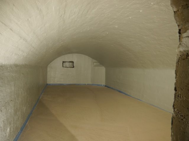 Leerer Raum mit weißen Wänden und gewölbter Decke. Hellbrauner Boden, kleines quadratisches Fenster.