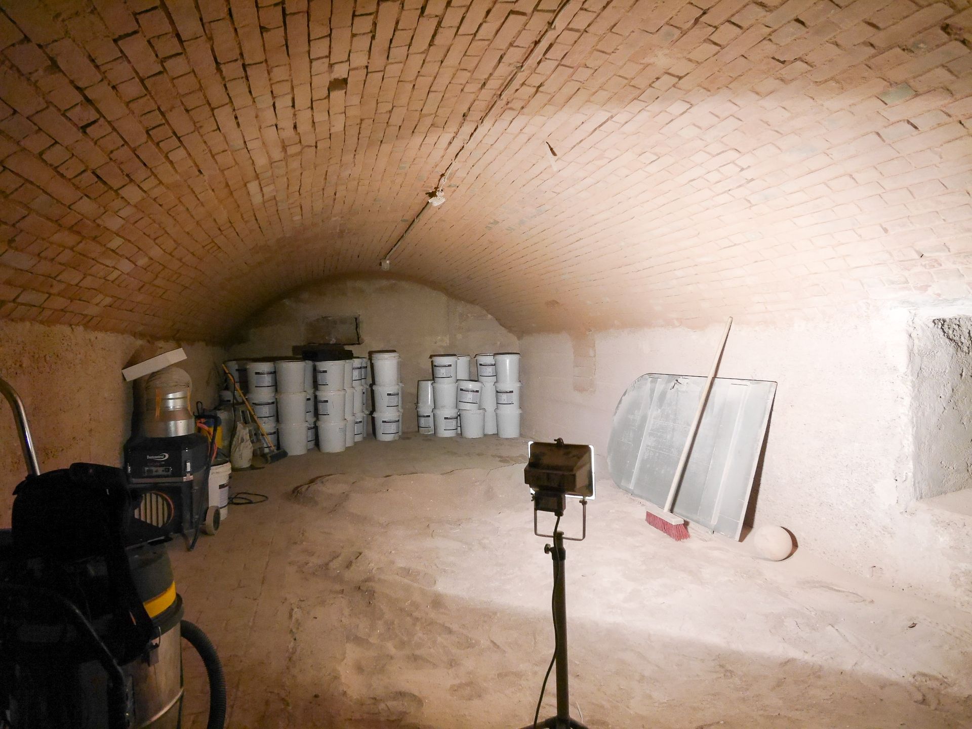 Keller mit Ziegelgewölbe, weißen Fässern, Werkzeugen und Scheinwerfern. Schwach beleuchteter, unterirdischer Lagerraum.