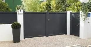Portail double noir moderne avec piliers blancs et arbustes en pot à l'entrée d'une maison