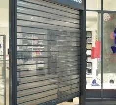Grille de sécurité en métal noir fermée devant une vitrine présentant des étagères et des vêtements à l'intérieur.