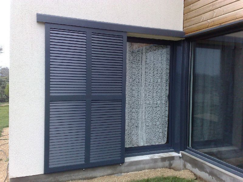 Fenêtre à volets bleus à côté d'une porte vitrée sur la façade d'une maison blanche