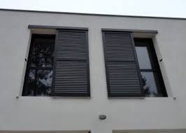 Façade blanche d'un bâtiment avec deux fenêtres et des volets sombres, vue d'en bas