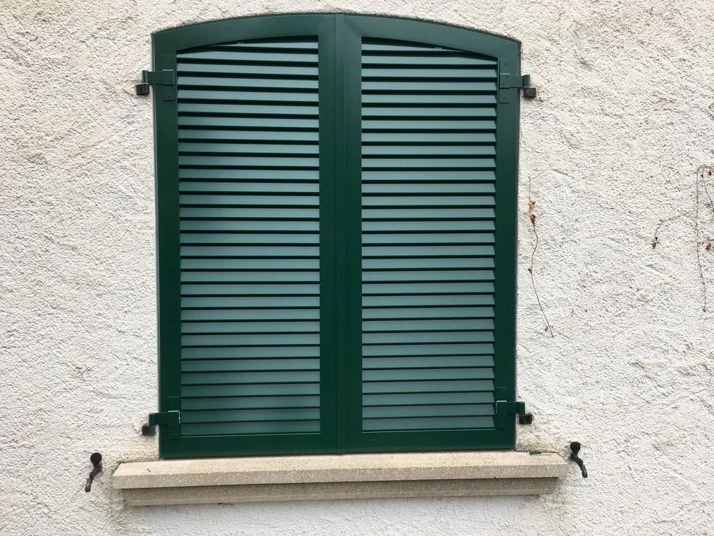Fenêtre à volets verts encastrée dans un mur en stuc blanc