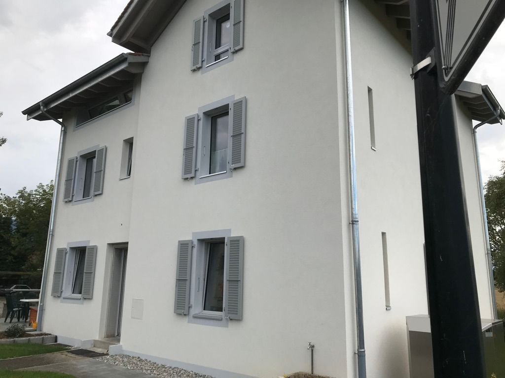 Extérieur d'une maison blanche avec des volets gris et un toit foncé, vu de côté.
