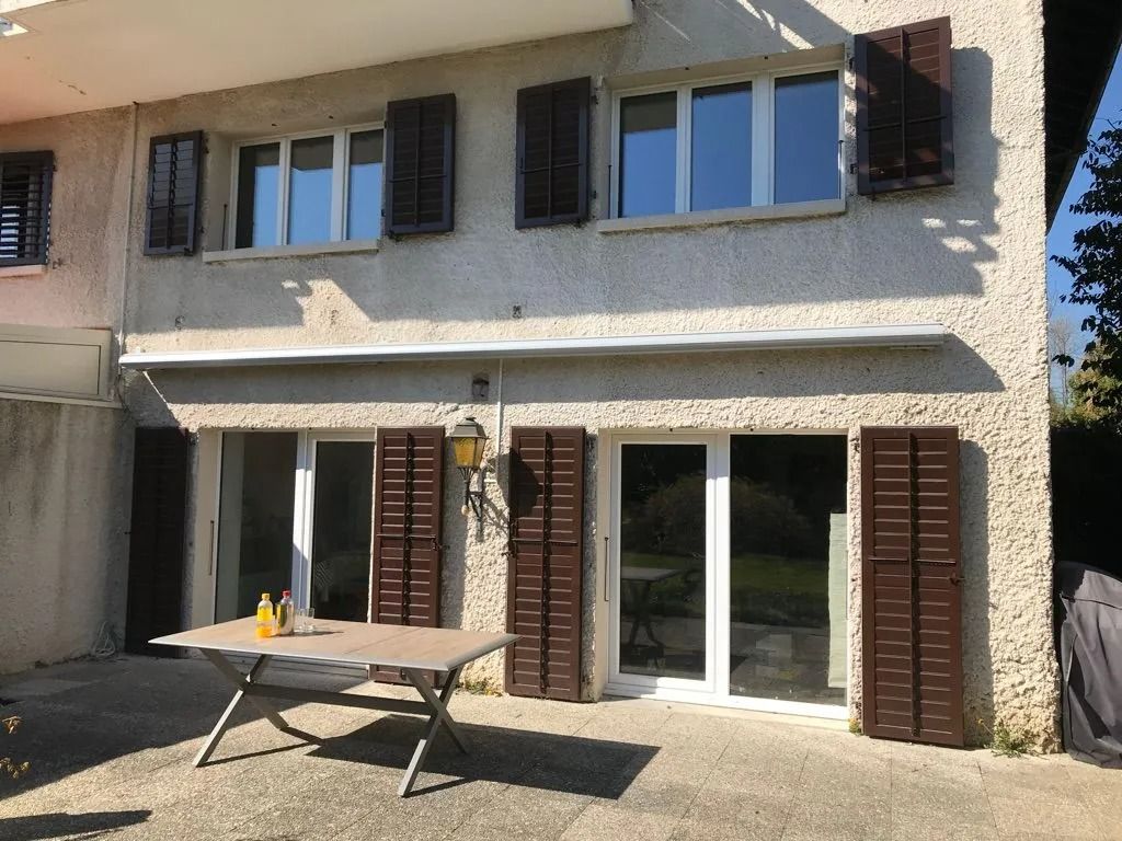 Maison à deux étages avec volets et portes vitrées, table de patio devant, par une journée ensoleillée