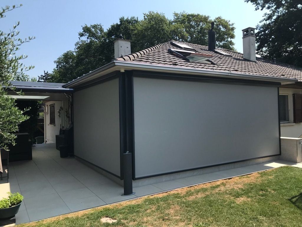 Vue latérale de l'arrière d'une maison moderne aux murs gris, au toit de tuiles et à l'allée menant à une terrasse.
