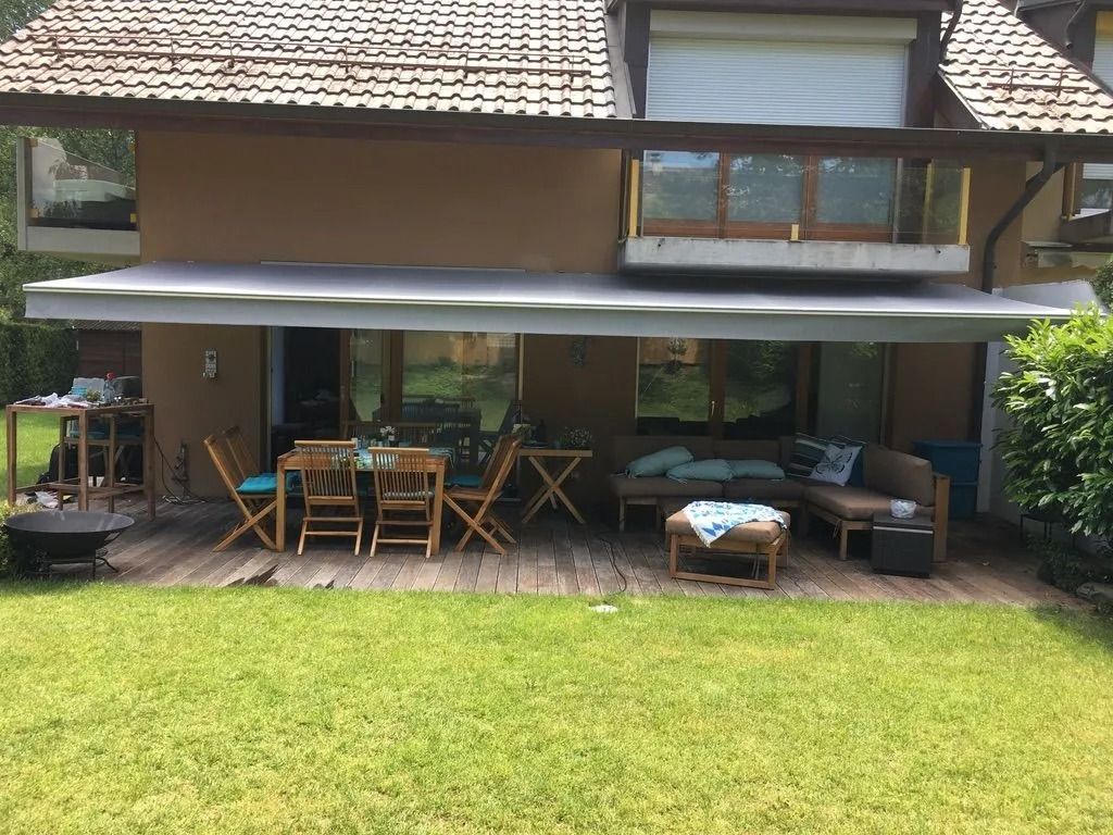 Terrasse arrière avec auvent, table et chaises en bois, canapé et pelouse verte devant une maison
