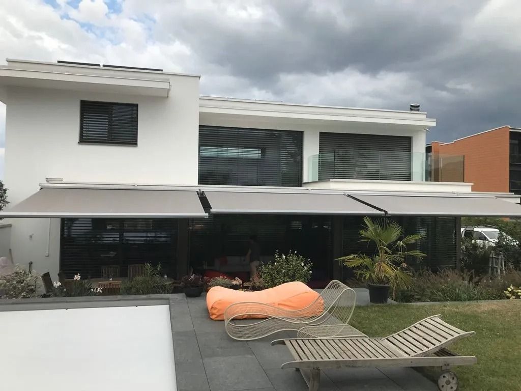 Maison moderne blanche de deux étages avec patio couvert, chaises longues et ciel nuageux