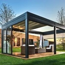 Pavillon moderne en verre à cadre noir avec terrasse aménagée sur une pelouse au coucher du soleil