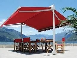 Table de patio rouge sous un grand parasol rouge sur une plage avec des montagnes et de l'eau en arrière-plan