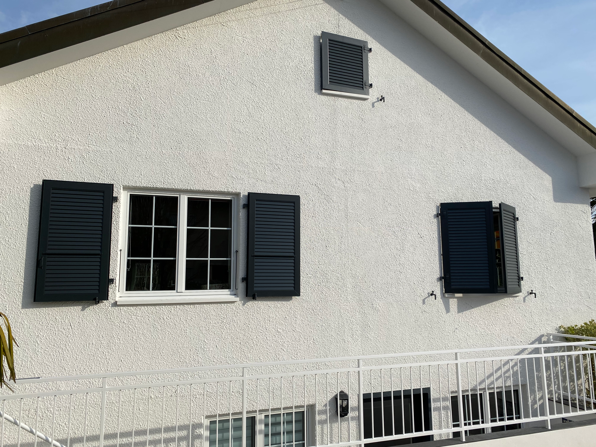 Extérieur d'une maison blanche avec des volets foncés, une fenêtre centrale et une balustrade blanche à l'avant.