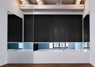 Pièce minimaliste vide avec de grands stores noirs, des murs blancs et un parquet.