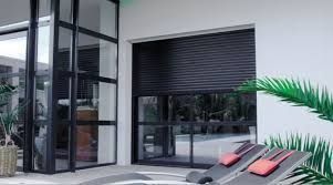 Terrasse moderne avec chaises longues près de grandes portes vitrées et un store noir enroulé.