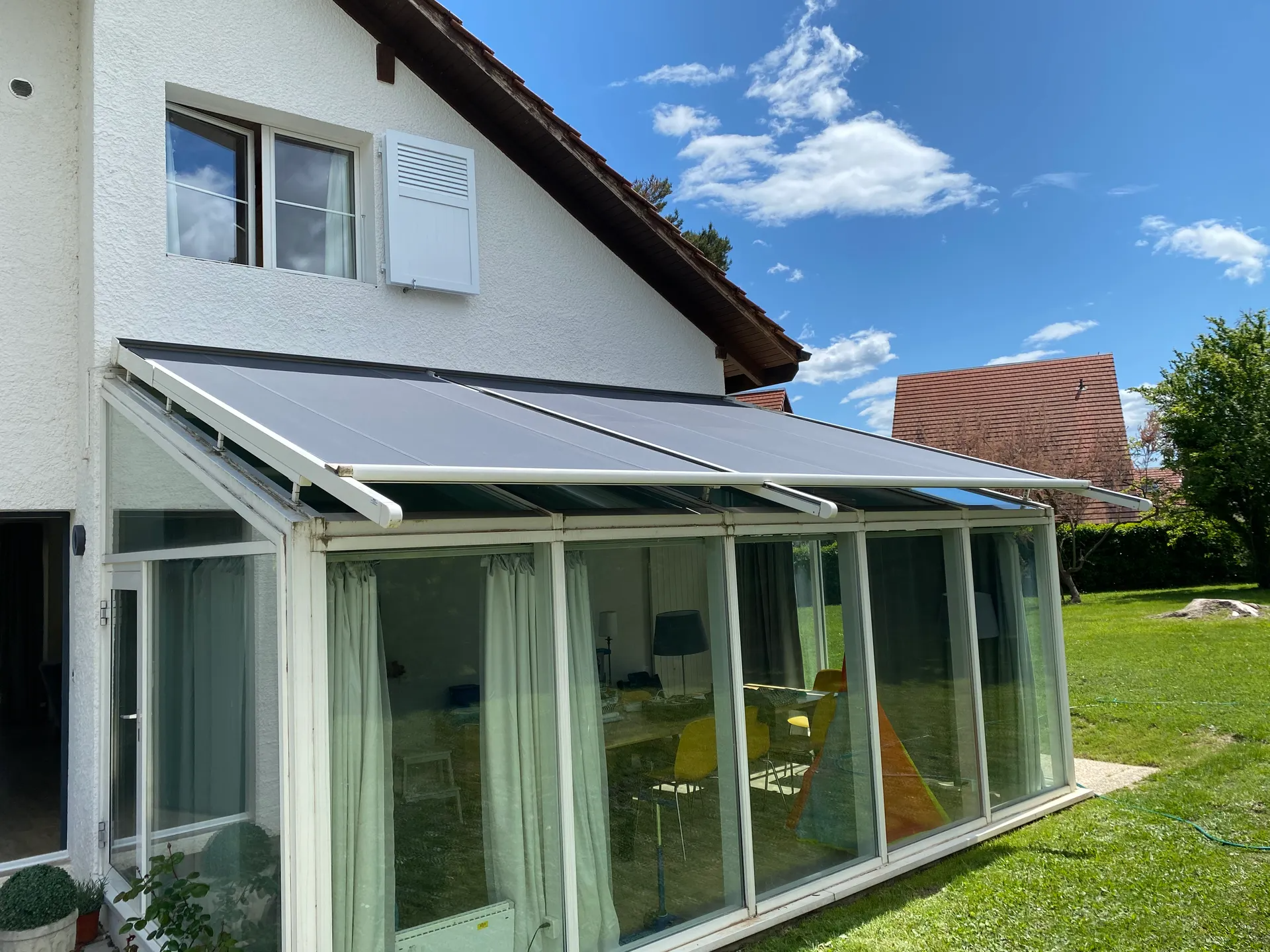 Patio vitré avec store rétractable à côté d'une maison blanche par une journée ensoleillée