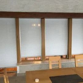 Fenêtres à cadre en bois avec stores blancs fermés au-dessus d'une table et de chaises en bois dans une pièce