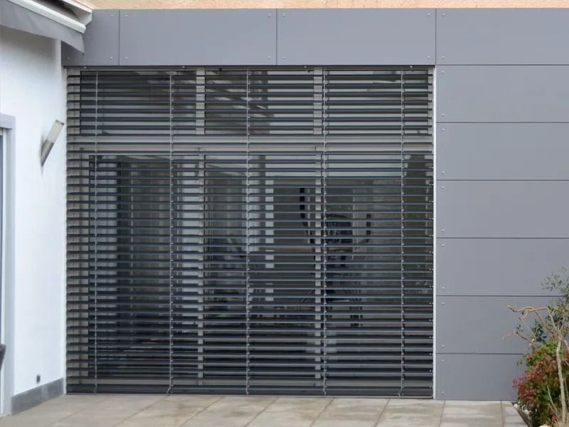 Façade d'immeuble moderne avec une grande entrée vitrée recouverte de stores horizontaux sombres