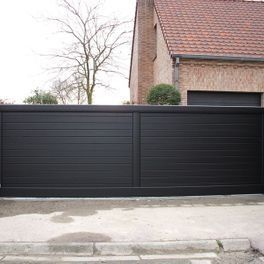 Portail d'allée en métal noir devant une maison en briques dans une rue résidentielle