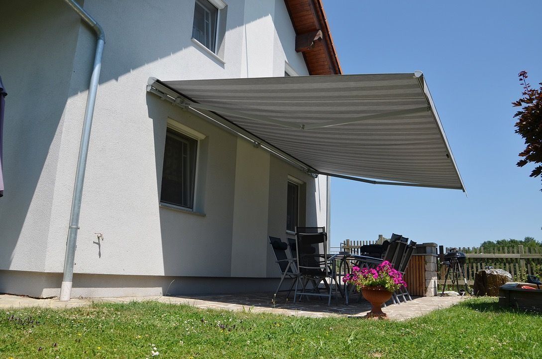 Terrasse de maison avec un auvent rayé, des chaises et des fleurs en pot à côté d'une pelouse