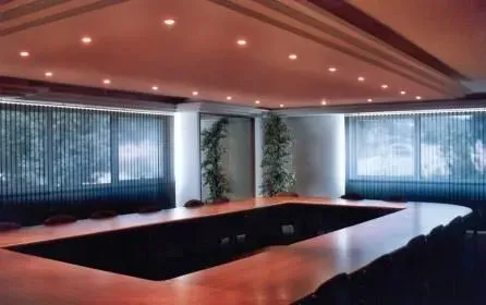 Salle de conférence moderne avec une longue table, un éclairage encastré et de grands stores.