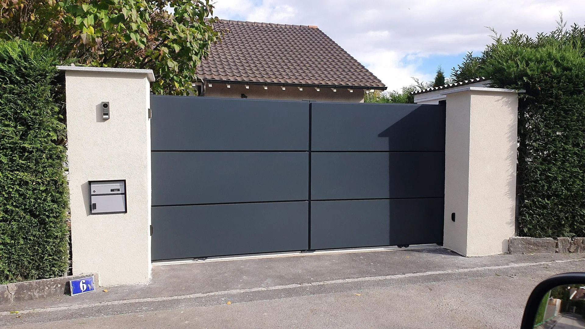 Portail moderne gris foncé entre des piliers blancs dans une allée résidentielle
