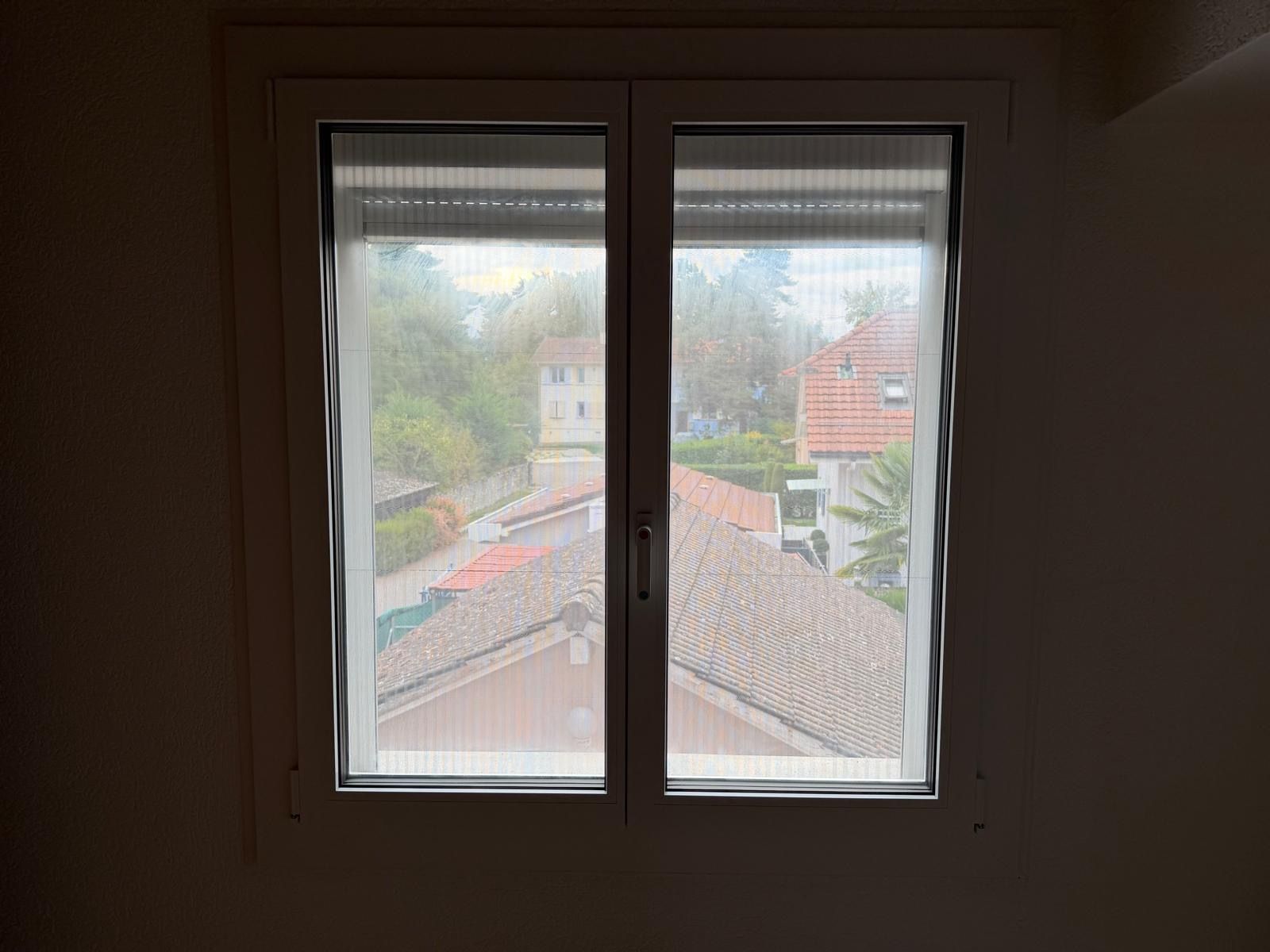 Portail coulissant blanc pour allée, adossé à un mur beige, avec une clôture blanche et des arbres en arrière-plan.