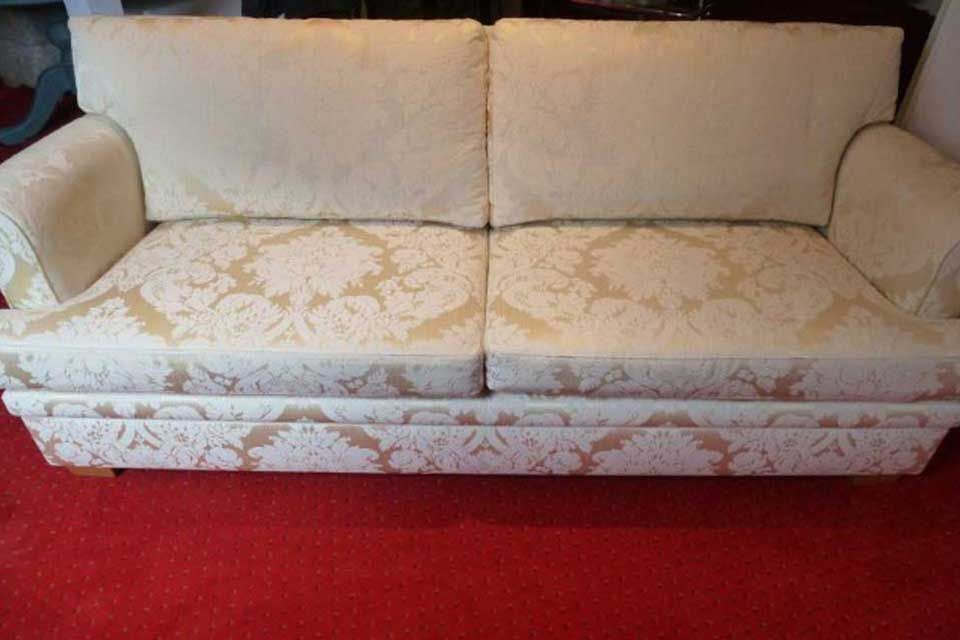 Cremefarbenes Zweisitzer-Sofa mit Blumenmuster auf einem roten Teppich.