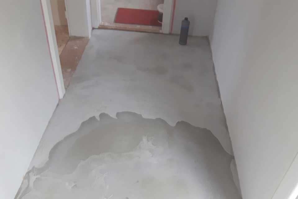 Frisch gegossener Betonboden in einem Flur, mit nassen Stellen und einer Flasche.