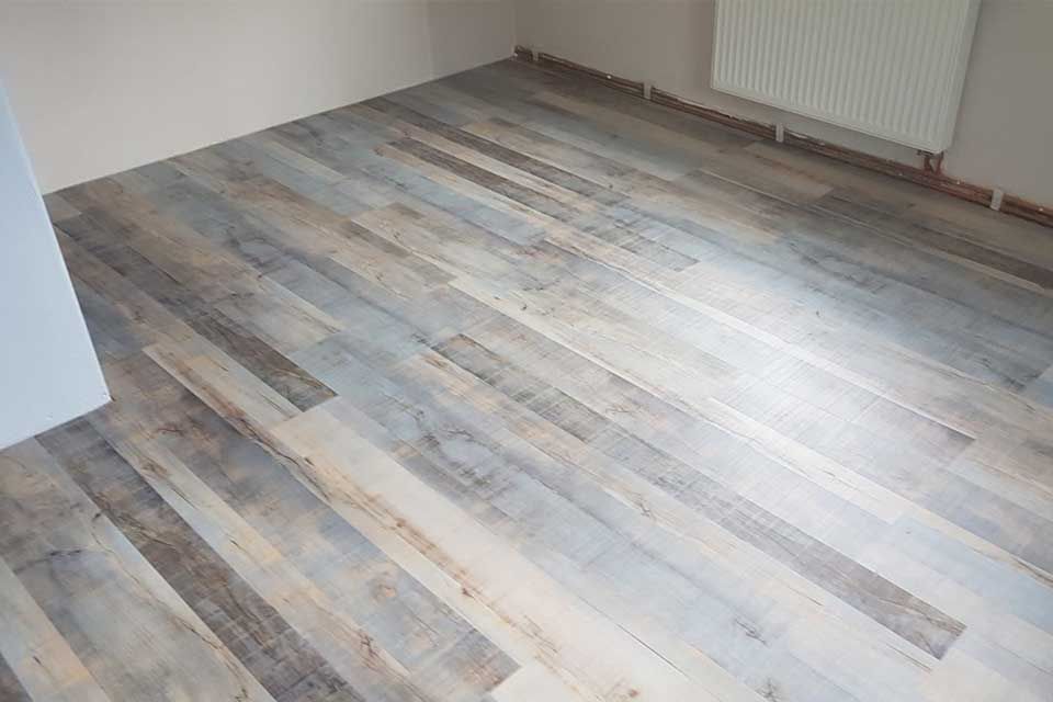 Holzdielenboden in einem Zimmer mit weißen Wänden und Heizkörper.