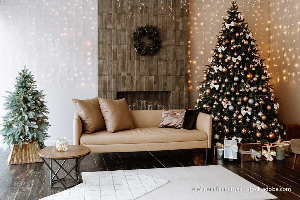 Wohnzimmer mit Weihnachtsdekoration: geschmückter Baum, Sofa, Kranz und Lichterketten.