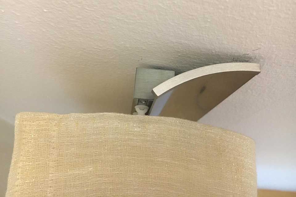 Beiger Lampenschirm mit einer gebogenen, weißen Leuchte, an einer weißen Decke montiert.