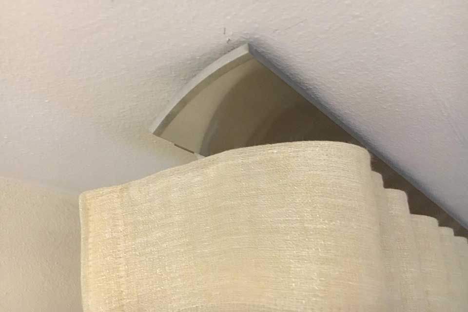 Beige Vorhänge hängen an einem geschwungenen, hellen Volant an einer weißen Decke.