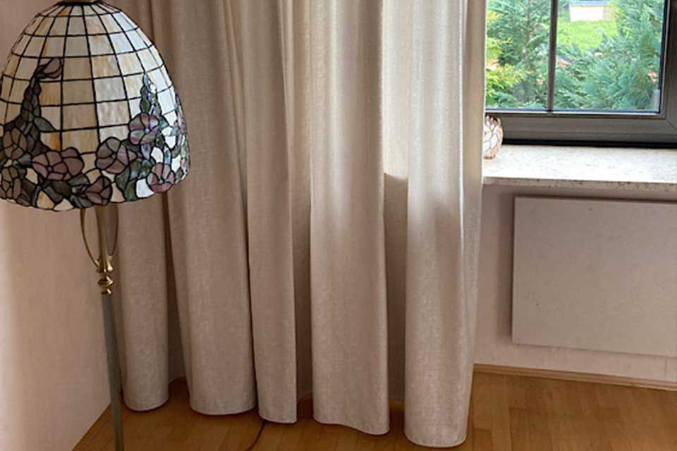 Eine Buntglaslampe neben hellen Vorhängen vor einem Fenster.