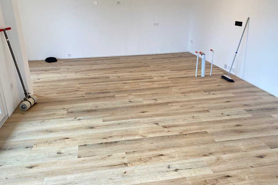 Frisch verlegter heller Holzboden in einem leeren Raum mit weißen Wänden. Werkzeuge sind sichtbar.