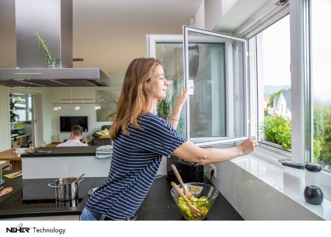 Frau öffnet ein Fenster in einer Küche mit Blick ins Grüne draußen.