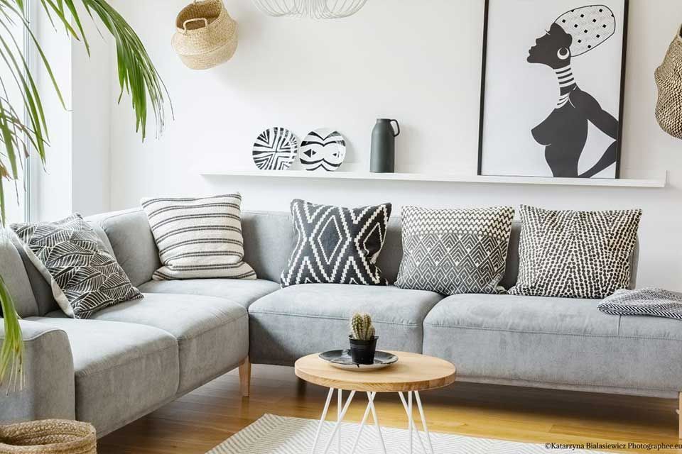 Graues Sofagarnitur mit dekorativen Kissen und Couchtisch aus Holz in einem hellen Wohnzimmer.