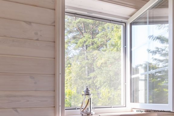 Offenes Fenster mit Fliegengitter, weißer Rahmen, helle Holzwände, Laterne auf der Fensterbank, Bäume draußen.