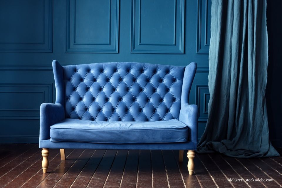 Blaues, büscheliges Samtsofa vor einer blau getäfelten Wand, mit blauem Vorhang und Holzboden.